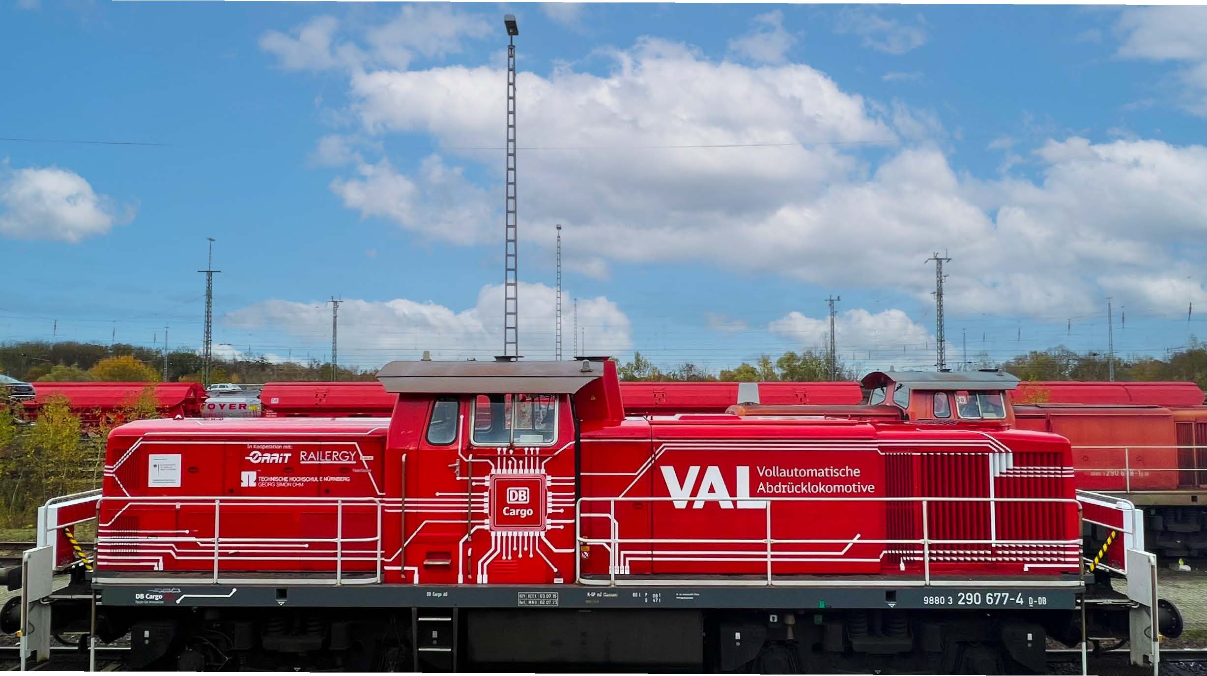 Side shot of a VAL train engine on the tracks, with other red trains in the background.
